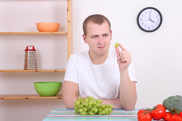 Junger attraktiver Mann mit grüner Traube in der Küche
