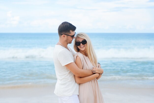 Junger attraktiver Mann und Frau in der Liebe gehen und umarmen auf weißem Sand und azurblauem Meer. Reisen, Flitterwochen