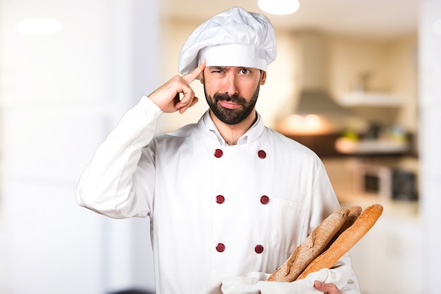 Junger Bäcker hält Brot und Denken in der Küche