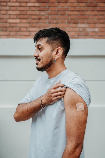 Junger bärtiger argentinischer Mann, der das Pflaster auf seinem Arm zeigt, nachdem er gegen COVID19 geimpft wurde