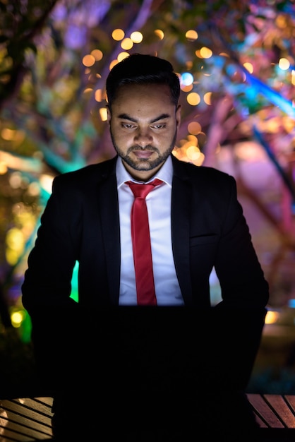 Junger bärtiger indischer Geschäftsmann gegen Ansicht der Stadt bei Nacht