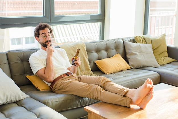 Junger bärtiger kühler Mann, der auf einer Couch zu Hause sitzt