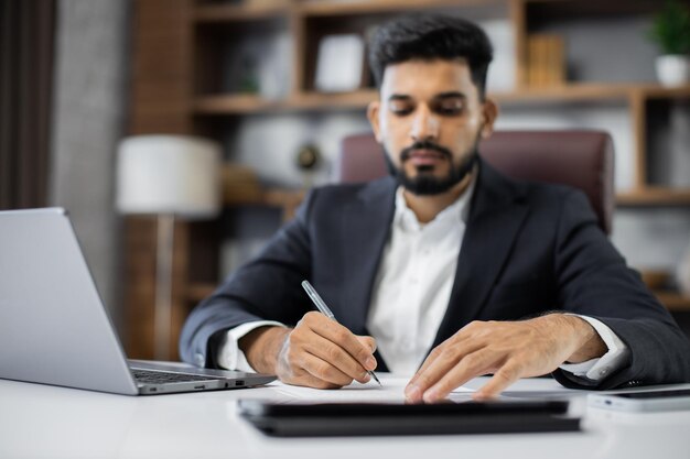 Junger bärtiger männlicher Buchhalter, der vom modernen Büro aus mit Laptop arbeitet