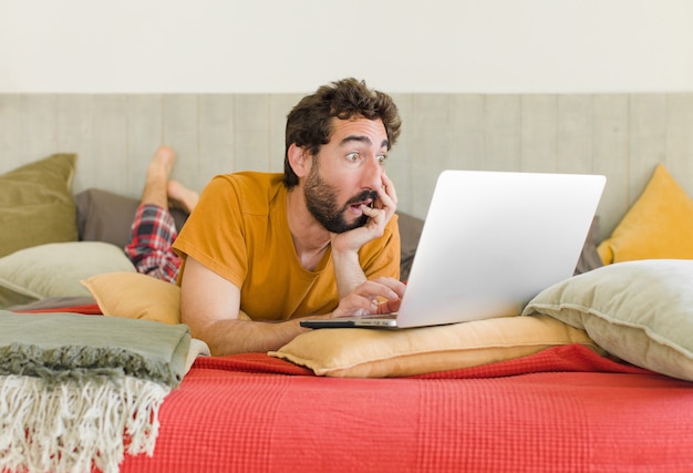 Junger bärtiger Mann auf einem Bett mit einem Laptop