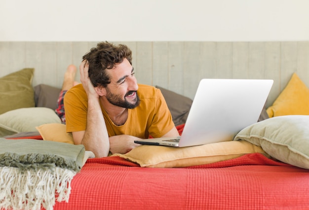 Junger bärtiger Mann auf einem Bett mit einem Laptop