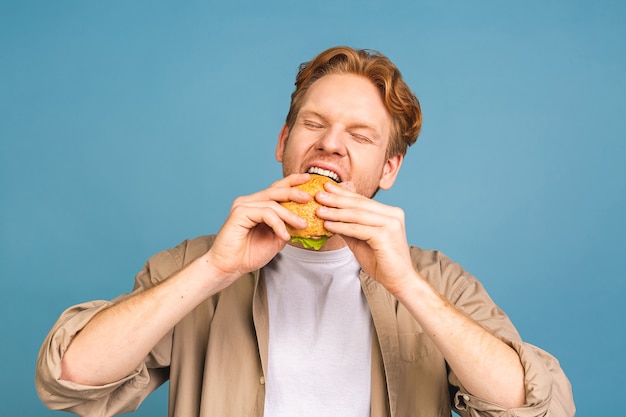 junger bärtiger mann, der ein stück hamburger hält. Student isst Fast Food