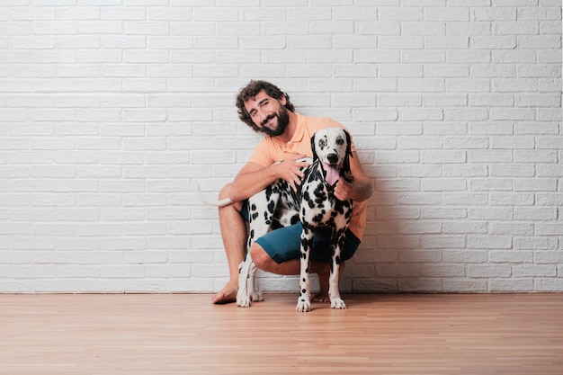 Junger bärtiger Mann mit einem dalmatinischen Hund gegen weiße Backsteinmauer