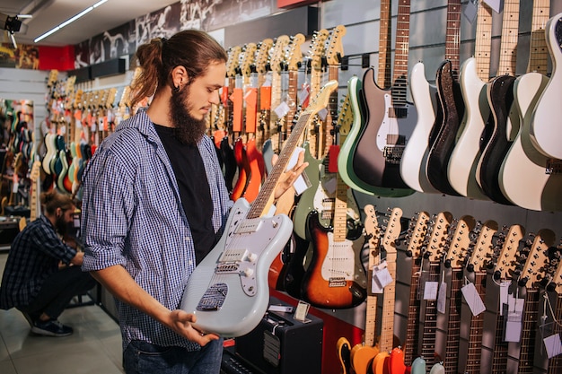 Junger bärtiger Musiker hält hellblaue E-Gitarre in Händen. Er sieht es an.