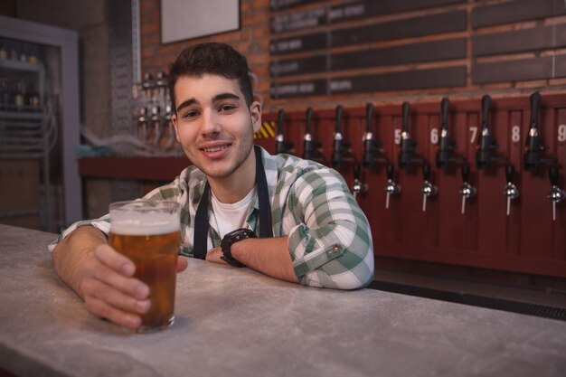 Junger barkeeper, der freudig lächelt und glas über köstlichem hellem bier, kopierraum dient