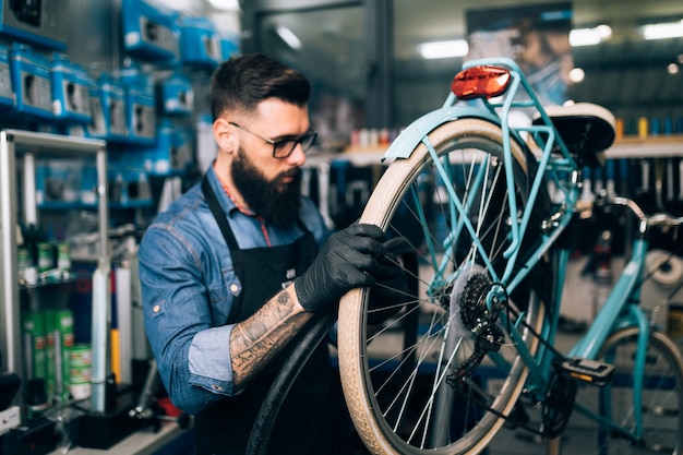 Junger Bartfahrradmechaniker, der Fahrräder in einer Werkstatt repariert.