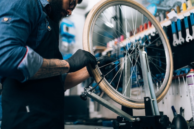 Foto junger bartfahrradmechaniker, der fahrräder in einer werkstatt repariert.