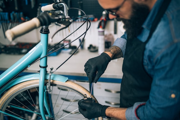 Junger Bartfahrradmechaniker, der Fahrräder in einer Werkstatt repariert.