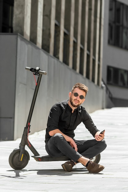 Junger Bartmann auf Elektroroller mit Smartphone in der Hand