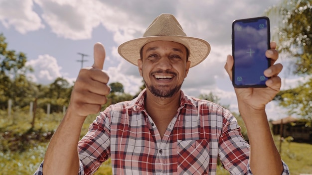 Junger Bauer mit Hut lächelt in die Kamera und zeigt Smartphone mit Chroma-Key-Bildschirm