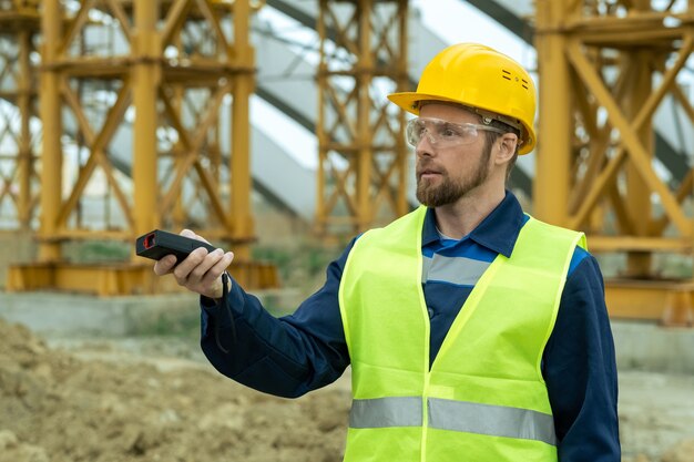 Junger Baumeister in Uniform und Bauarbeiterhelm, der auf der Baustelle arbeitet