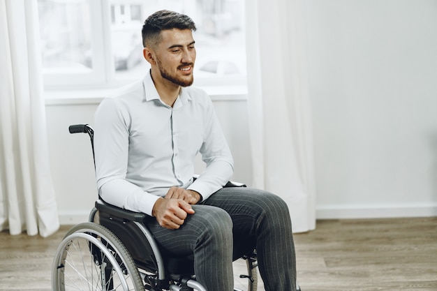 Junger behinderter Mann, der in einem Rollstuhl nahe dem Fenster sitzt