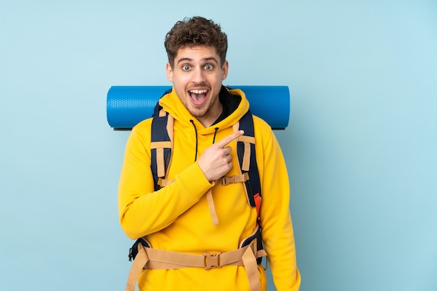 Junger Bergsteigermann mit einem großen Rucksack lokalisiert auf blau zeigendem Finger zur Seite