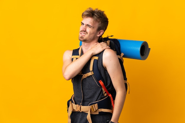 Junger Bergsteigermann mit einem großen Rucksack lokalisiert auf gelbem Hintergrund, der unter Schmerzen in der Schulter leidet, weil er sich bemüht hat