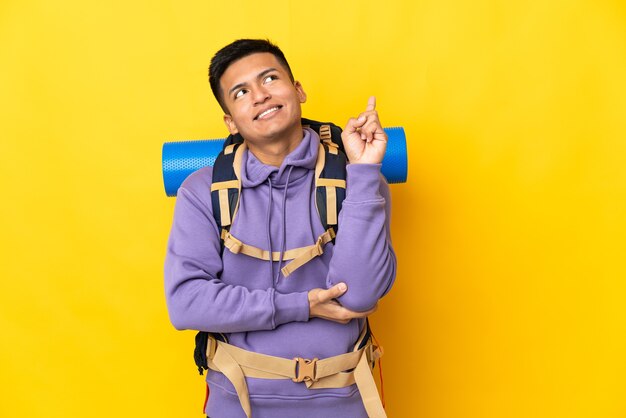 Junger Bergsteigermann mit einem großen Rucksack lokalisiert auf gelber Wand, die eine große Idee aufzeigt