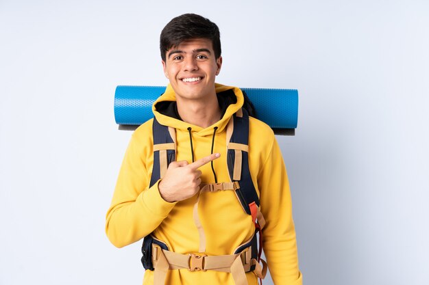 Junger Bergsteigermann mit einem großen Rucksack über blauer Wand, der Finger zur Seite zeigt