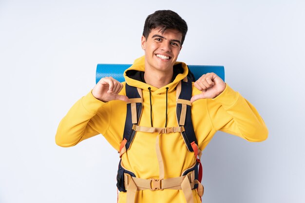 Junger Bergsteigermann mit einem großen Rucksack über isoliertem Blau stolz und selbstzufrieden