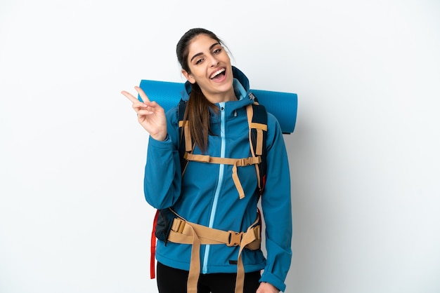 Junger Bergsteigermann mit einem großen Rucksack über isoliertem Hintergrund, der lächelt und Victory-Zeichen zeigt