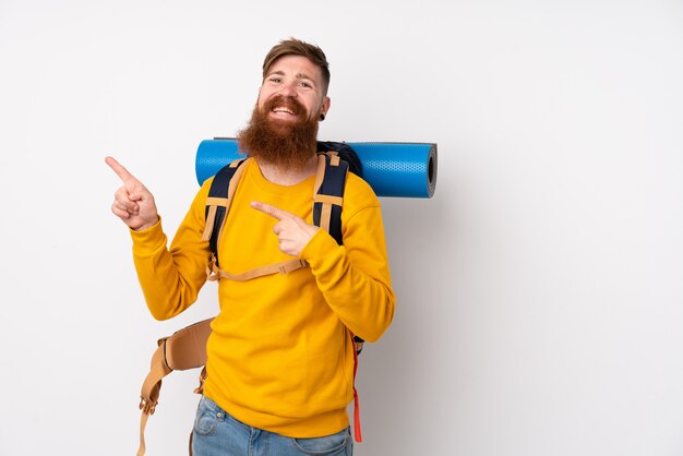 Junger Bergsteigermann mit einem großen Rucksack über isoliertem weißem Zeigefinger zur Seite