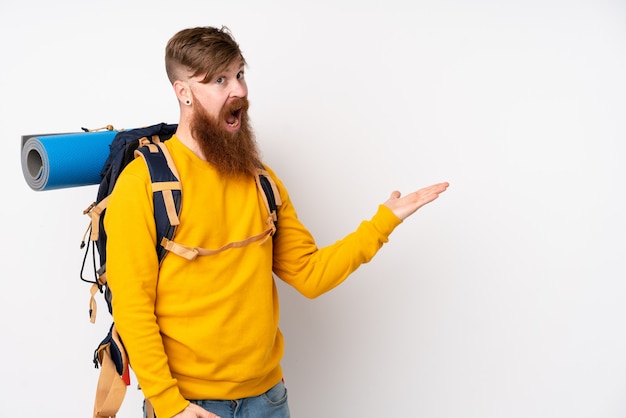 Junger Bergsteigermann mit einem großen Rucksack über isolierter weißer Wand, die Hände zur Seite ausdehnt, um einzuladen, zu kommen