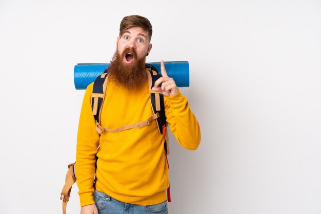 Junger Bergsteigermann mit einem großen Rucksack über isolierter weißer Wand, die mit dem Zeigefinger eine große Idee zeigt