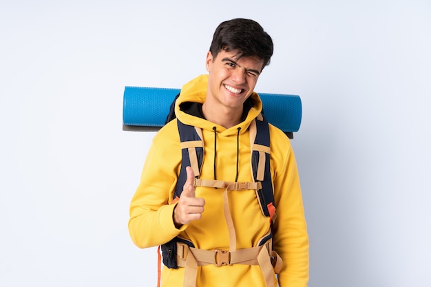 Junger Bergsteigermann mit einem großen Rucksack über lokalisiertem blauem Hintergrund zeigt Finger auf Sie