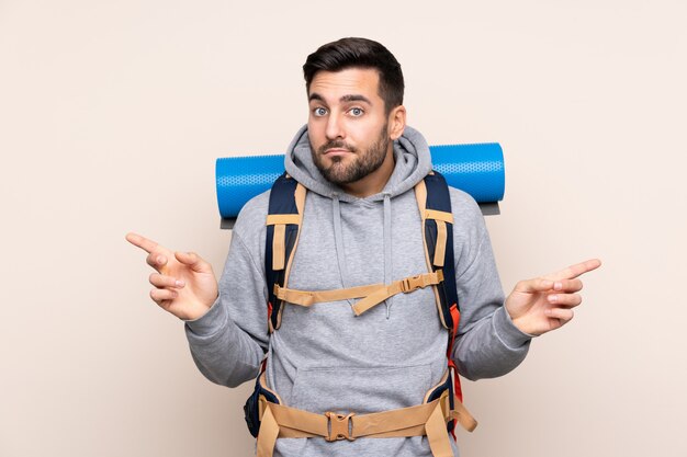 Junger Bergsteigermann mit einem großen Rucksack über lokalisierter Wand zeigend auf die Seitenteile, die Zweifel haben