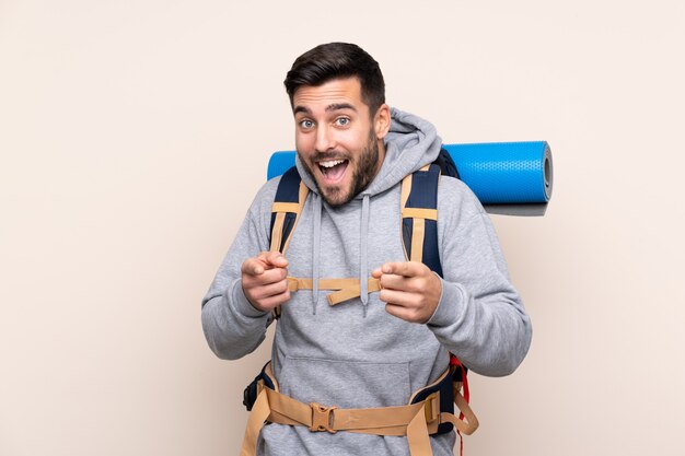 Junger Bergsteigermann mit einem großen Rucksack zeigt Finger auf Sie