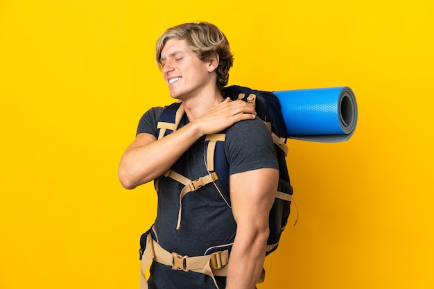Junger Bergsteigermann über isolierter gelber Wand, die unter Schmerzen in der Schulter leidet, weil er sich bemüht hat