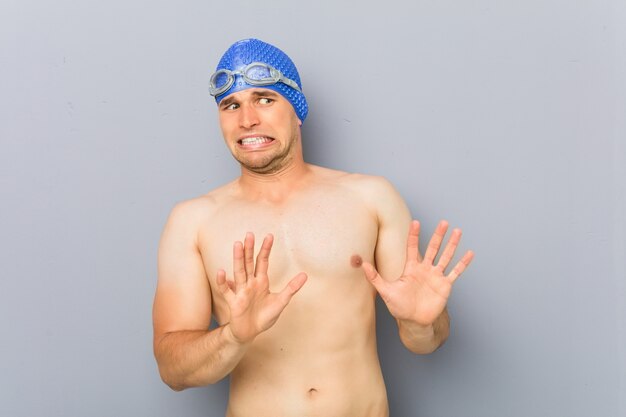 Junger Berufsschwimmermann, der jemand zeigt eine Geste des Ekels zurückweist.