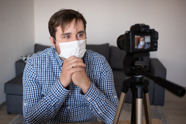 Junger Blogger mit Videoaufzeichnung zu Hause, während zu Hause auf Coronavirus-Quarantäne, Coronavirus, Krankheit, Infektion, Quarantäne, medizinische Maske bleiben