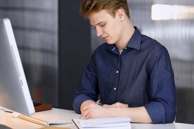 Junger blonder geschäftsmann, der mit computer arbeitet. startup-geschäft bedeutet, hart und ohne zeitdruck für den erfolg zu arbeiten.