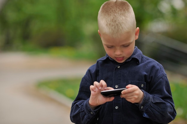 junger blonder Junge, der Videospiele im Freien im Park spielt