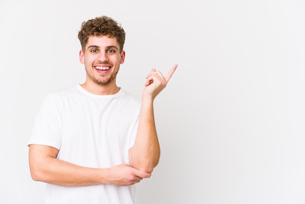 Junger blonder kaukasischer Mann des lockigen Haares isoliert lächelnd, der mit Zeigefinger weg zeigt.