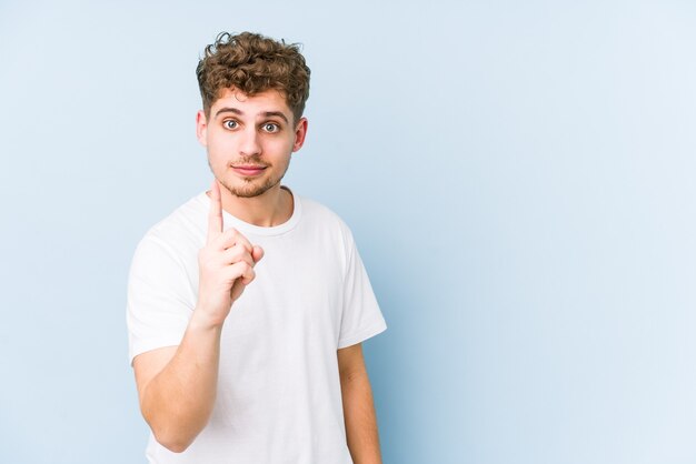 Junger blonder kaukasischer Mann des lockigen Haares lokalisiert, der Nummer eins mit Finger zeigt.