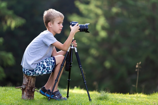 Junger blonder Kinderjunge, der auf dem Baumstumpf macht Foto sitzt