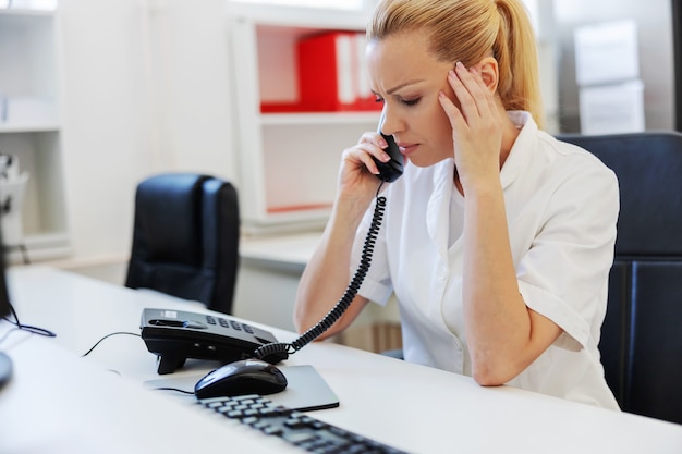 Junger blonder laborassistent, der kopf hält und schlechte nachrichten am telefon erzählt.