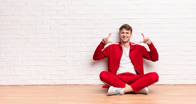 Junger blonder Mann, der auf dem Boden sitzt