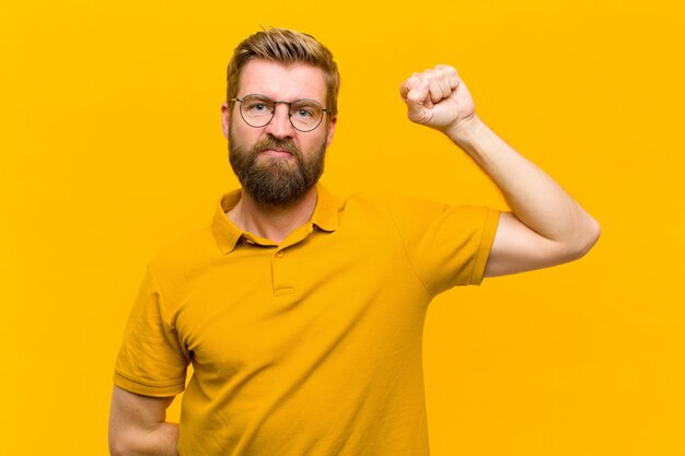 Junger blonder Mann, der ernst, stark und rebellisch sich fühlt, Faust oben anhebt, protestiert oder für Revolution kämpft