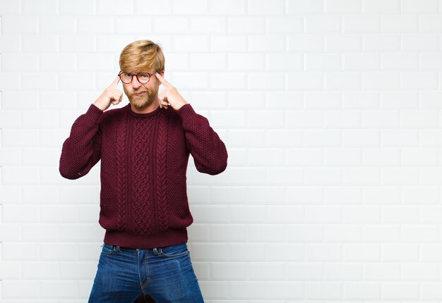 Junger blonder Mann, der konzentriert schaut und über eine Idee nachdenkt und sich eine Lösung für eine Herausforderung oder ein Problem gegen Vintage-Fliesenwand vorstellt