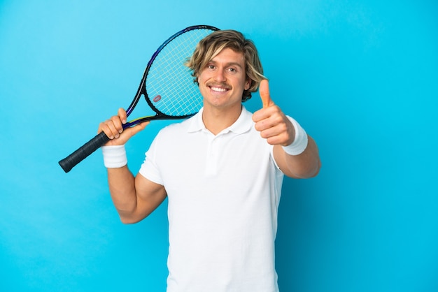 Junger blonder Mann isoliert, der Tennis und mit dem Daumen nach oben spielt