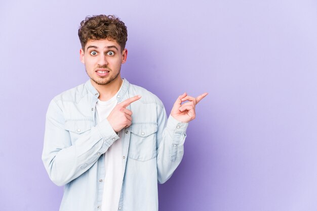 Junger blonder Mann mit lockigem Haar, der mit Zeigefingern schockiert zeigte