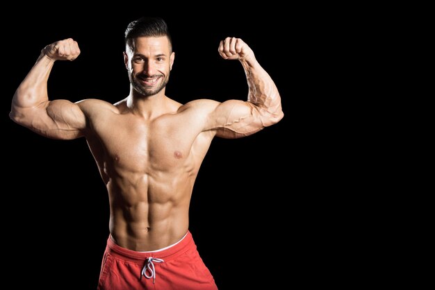 Junger Bodybuilder, der Muskeln biegt, isolieren auf schwarzem Blackground