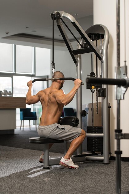Junger Bodybuilder, der schwere Übung für den Rücken auf der Maschine macht