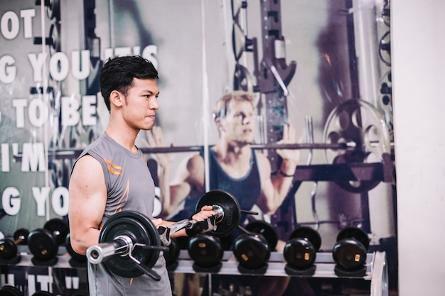 Junger Bodybuilder trainiert, indem er einen Dummkopf in der Turnhalle anhebt.