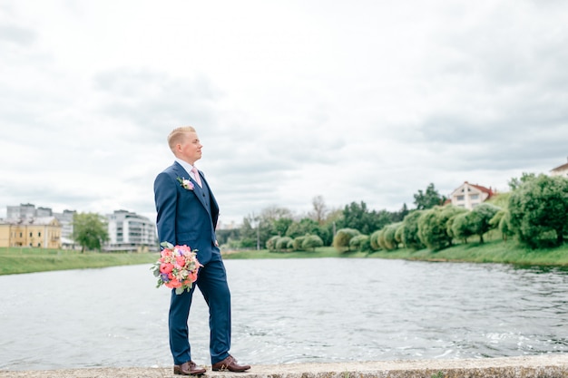 Junger Bräutigam mit Blumenstrauß in seiner Hand, die draußen mit See aufwirft